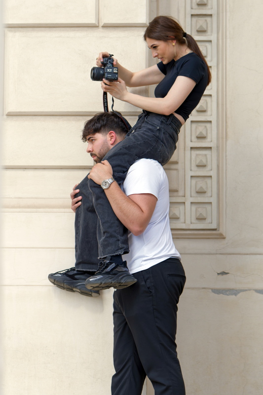 Girl photographing while seated on another person's shoulders.